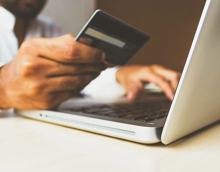 A person holding their credit card while using a laptop.